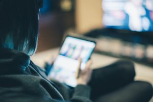 Young woman relaxing with tablet on sofa in front of TV